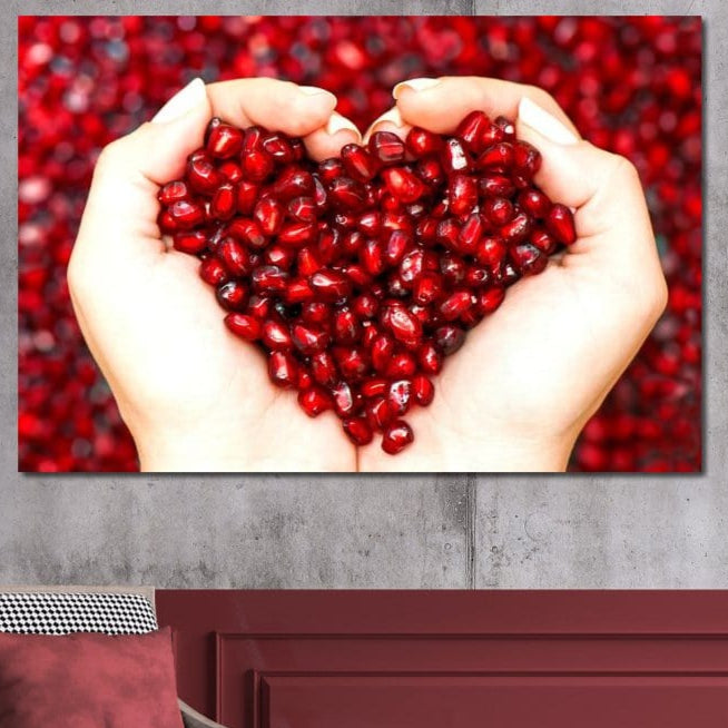tablou canvas cu seminte de rodie, cuprinse intre doua maini, pe fundal rosu