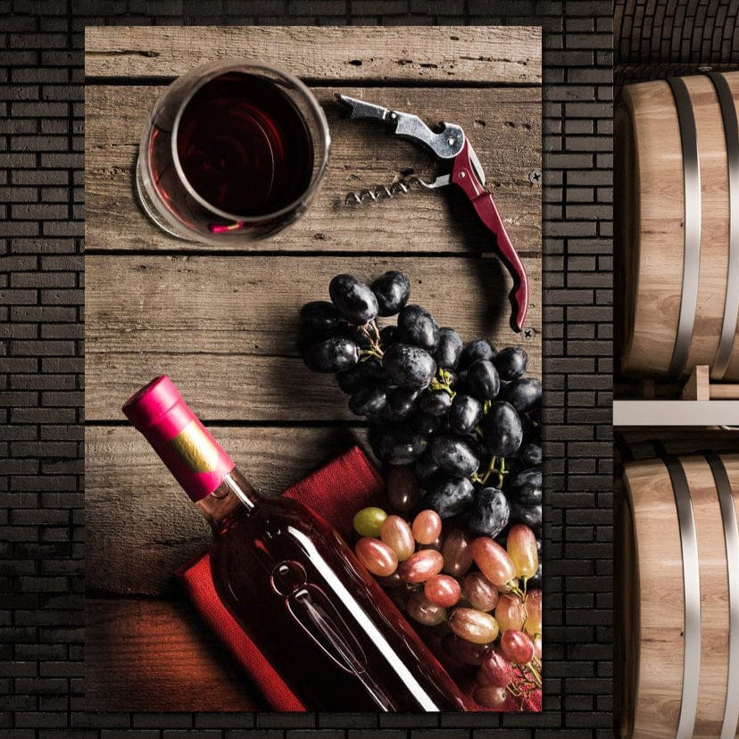 tablou canvas cu o sticla si un pahar de vin rosu, alaturi de struguri albi si negri, pe o masa de lemn, intr-un peisaj traditional