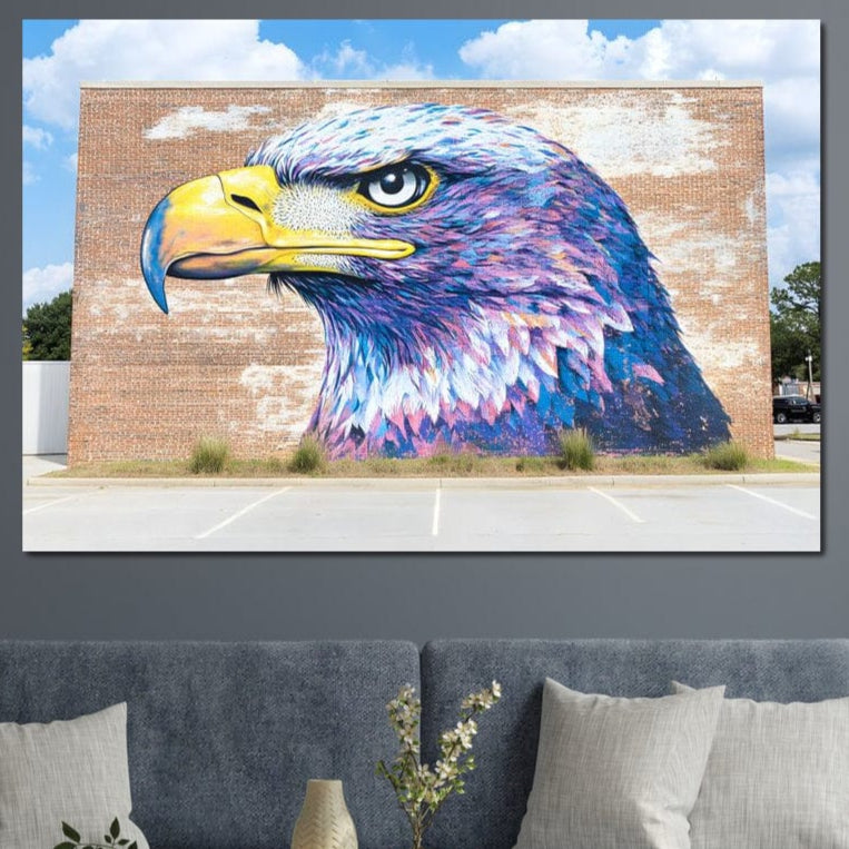 tablou canvas cu un vultur in nuante electrice de violet, albastru si galben pictat in stil mural pe un zid de caramida