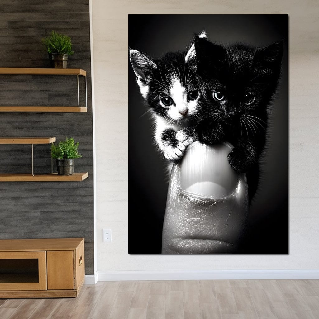 tablou canvas cu doua pisicute mici, alb si negru, agatate de un deget, pe fundal intunecat