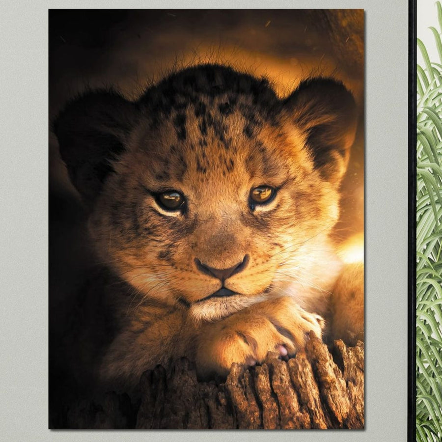 Un portret apropiat al unui pui de leu care se odihnește pe un trunchi de copac, scăldat în lumina caldă a răsăritului, imprimat ca Tablou Canvas Premium LuxCanva® M1377 - Micul Rege: perfect pentru birou, camera de zi sau camera copiilor. Vegetația evidențiază partea dreaptă; fundalul este întunecat.