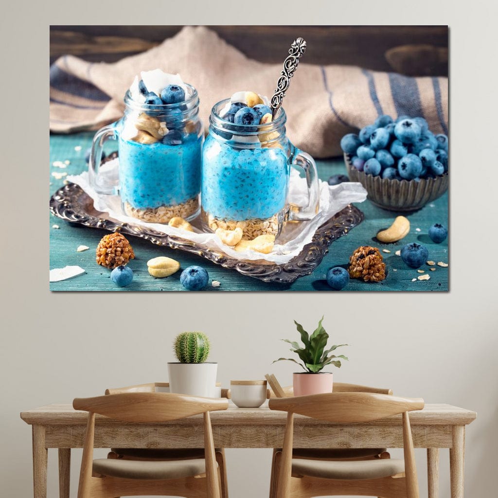 tablou canvas cu doua deserturi cu seminte de chia, afine si alune, pe o tava argintie, pe o masa albastru - turcoaz