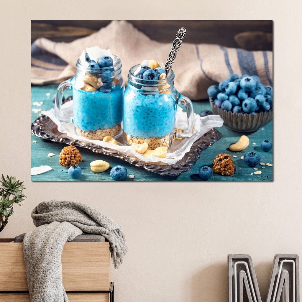 tablou canvas cu doua deserturi cu seminte de chia, afine si alune, pe o tava argintie, pe o masa albastru - turcoaz