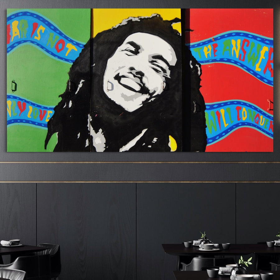 Tabloul LuxCanva® Tablou Canvas Premium B1116, The Great Bob Marley, îl prezintă pe muzicianul vesel pe roșu, galben și verde vibrante. Afișat deasupra unei zone de luat masa moderne, acesta poartă citatul: "Războiul nu este răspunsul, doar dragostea va învinge.