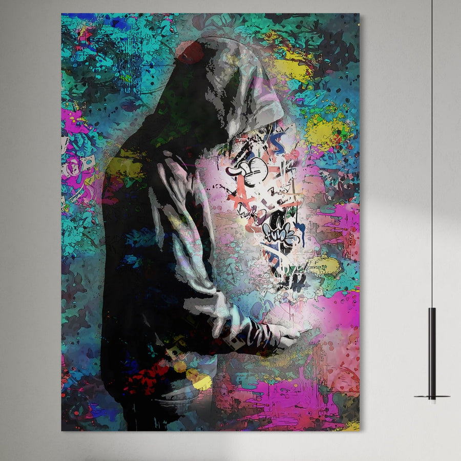 Un tânăr cu o jachetă cu glugă stă lângă un perete graffiti vibrant, stropit cu roz, albastru, galben și verde - capturând stilul urban dinamic în Tablou Canvas Premium LuxCanva® B1101 "Grafitti Boy" pentru dormitoare sau camere de zi moderne.