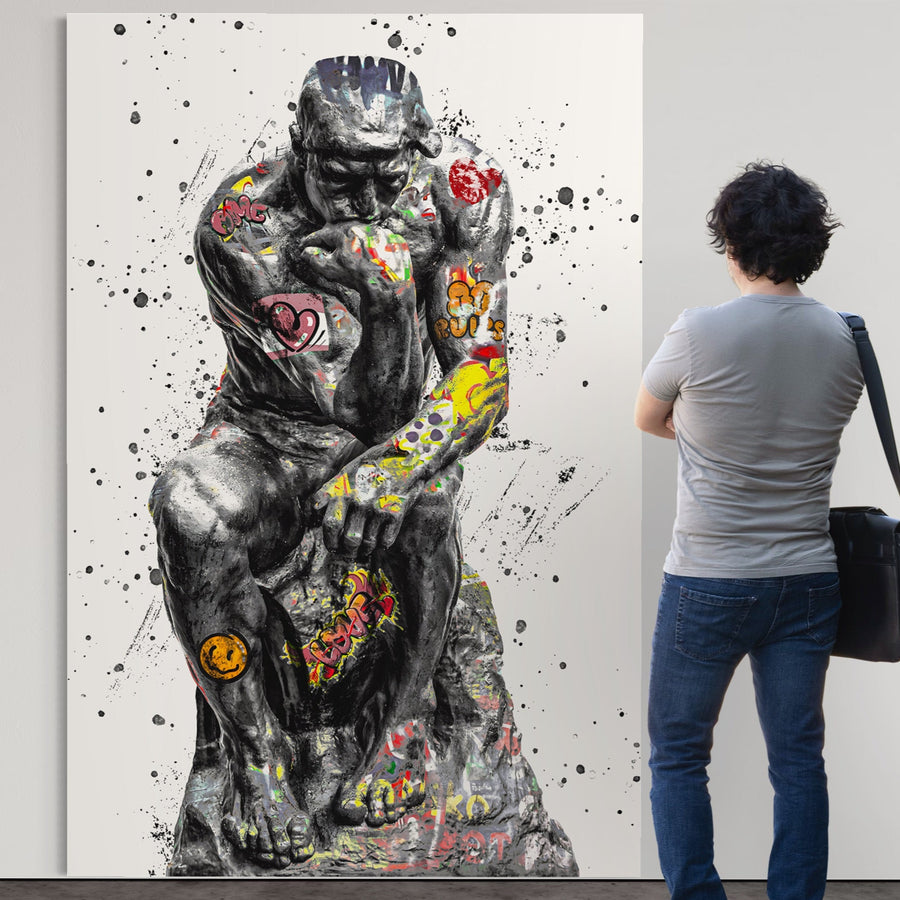 O persoană stă în fața Tablou Canvas Premium LuxCanva® B1044, Gânditorul - o imprimare abstractă, vibrantă, pe alb, care prezintă statuia clasică a lui Rodin împodobită cu graffiti, inimi și zâmbete, pentru un decor de living uimitor.