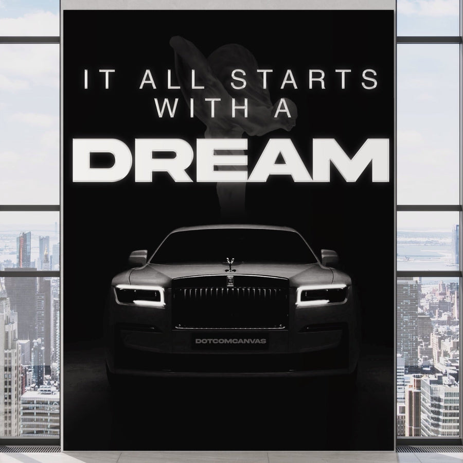 Un Rolls-Royce luxos se află în fața unui perete negru pe care scrie "IT ALL STARTS WITH A DREAM" (Totul începe cu o visare), ecou al eleganței Tablou Canvas Premium LuxCanva® B1038, o piesă decorativă inspirațională în alb și negru, cu zgârie-norii orașului văzuți prin ferestrele din apropiere.