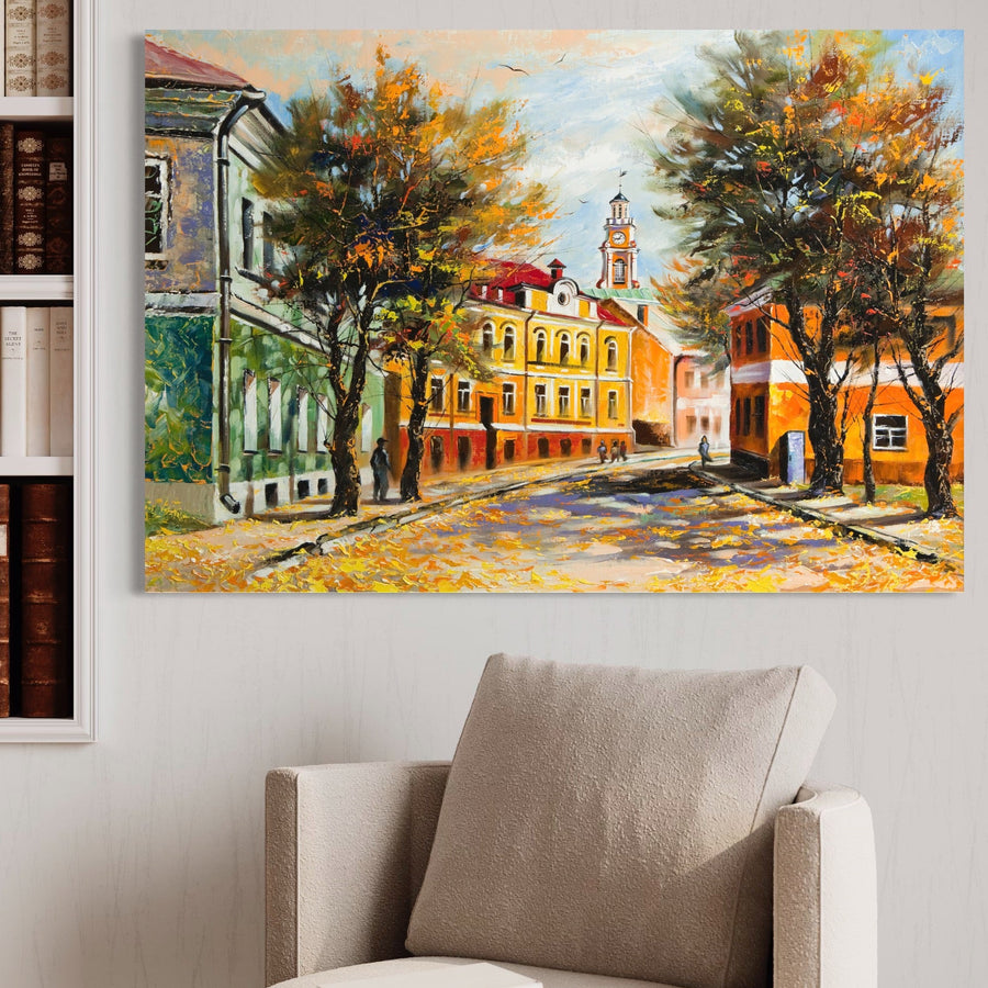 Tablou Canvas Premium LuxCanva® A1281, cu oameni, clădiri și stradă în culori vibrante de toamnă, decorează peretele alb deasupra unui fotoliu bej, aducând un plus de eleganță și culoare camerei.