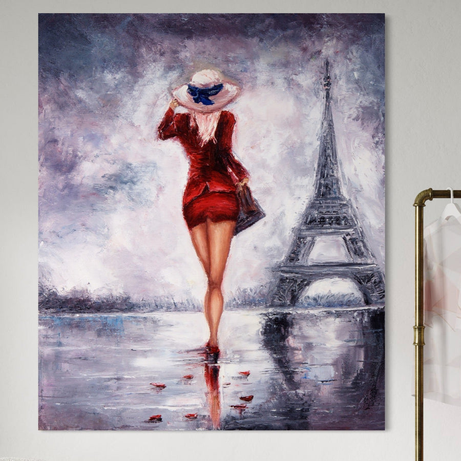 Tablou Canvas Premium LuxCanva® A1267 - Lady In Paris: femeie cu rochie roșie și pălărie, mergând spre Turnul Eiffel pe o suprafață umedă cu petale roșii sub un cer înnorat. Decor elegant pentru dormitor, culori vibrante.