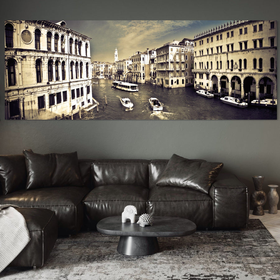 O cameră de zi modernă cu o canapea secțională din piele închisă, o măsuță de cafea rotundă neagră și o artă de perete LuxCanva® Tablou Canvas Premium A1260 Venetia Alb-Negru cu peisaje vibrante de canal. Tonurile neutre și decorul minimalist completează vibe-ul confortabil.