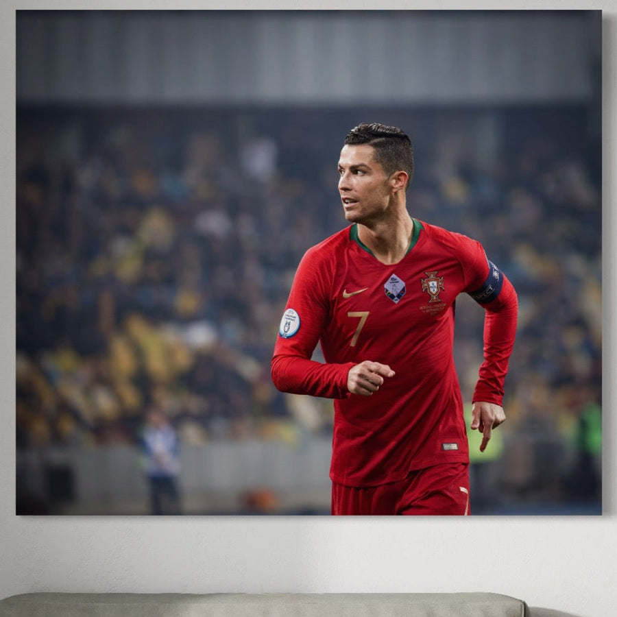 Tablou Canvas Premium C1053 de la LuxCanva® îl prezintă pe Cristiano Ronaldo în calitate de căpitan al Portugaliei în culori vibrante, o artă murală perfectă pentru o sală de jocuri sau un spațiu pentru copii, expusă deasupra unei canapele gri pentru un decor uimitor.