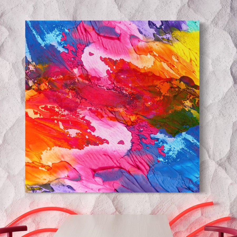 Tablou Canvas Premium LuxCanva® C1055 prezintă culori abstracte vibrante pe pânză, creând un accent viu deasupra unei mese și a două scaune roșii pe un perete alb texturat. Ideal pentru relaxare în camera de zi sau în dormitor.