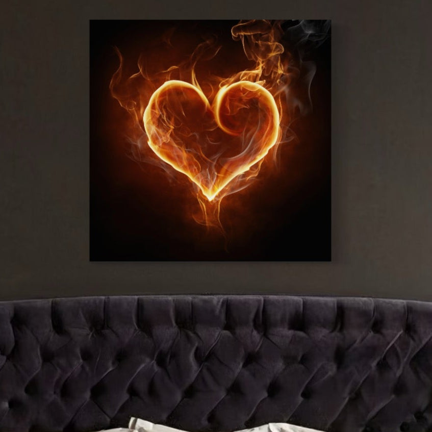 Tablou Canvas Premium LuxCanva® C1073 prezintă o inimă vibrantă în flăcări deasupra unei căpătâi întunecate, cu tonuri izbitoare de portocaliu și galben pe un fundal negru - ideală pentru camere de zi sau dormitoare.