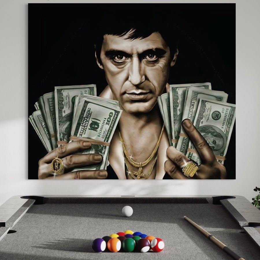 Sub tabloul LuxCanva® Tablou Canvas Premium A1226, care îl înfățișează pe Al Pacino în rolul lui Tony Montana din Scarface, ținând în mână dolari americani și purtând bijuterii din aur, se află o masă de biliard cu un tac și bile de biliard.