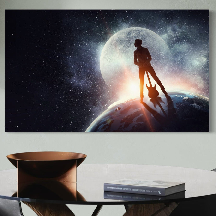 Tablou Canvas Premium C1085 de la LuxCanva®, "Cantaret In Varful Lumii", înfățișează un chitarist siluetat pe o planetă sub o lună strălucitoare și un cer înstelat, cu o masă, un bol și o carte în prim-plan - perfect pentru camera de zi sau dormitor.