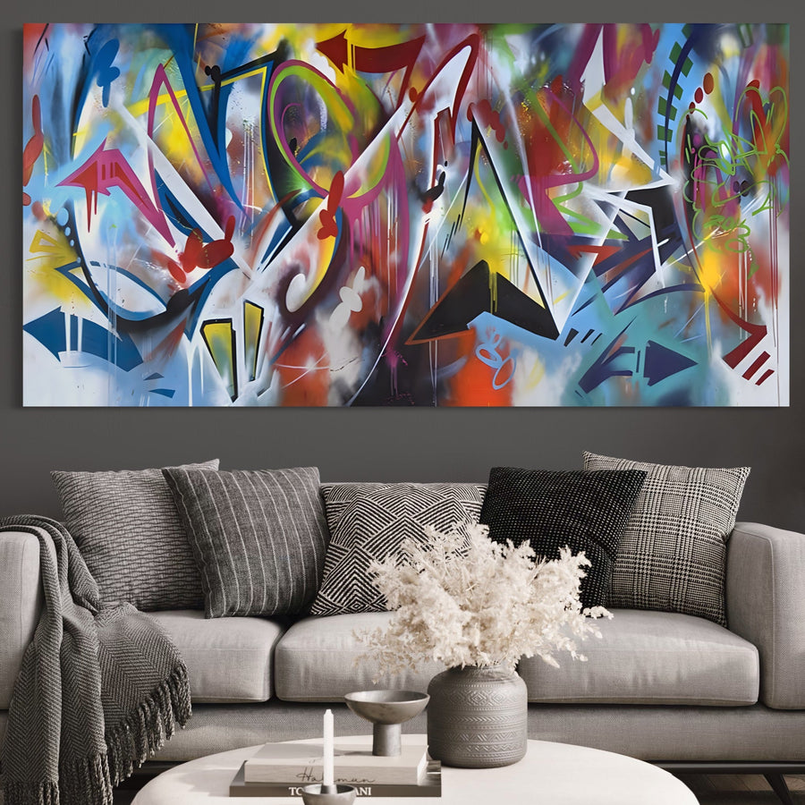 Un living modern cu o canapea gri deschis, perne albe și negre, un aranjament floral alb pe măsuța de cafea, iar Tablou Canvas Premium LuxCanva® A1210 Graffiti Blue adaugă culoare vibrantă și stil peretelui.