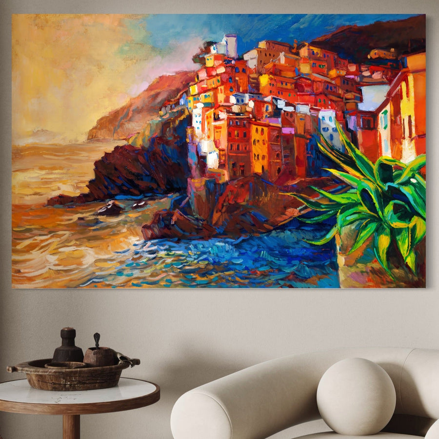 Tablou Canvas Premium LuxCanva® A1080 "Oras La Malul Marii" cu peisaj vibrant: case colorate pe stânci lângă mare, valuri dramatice și plantă verde, montat deasupra unei canapele albe pe perete bej. Calitate premium de la LuxCanva®.