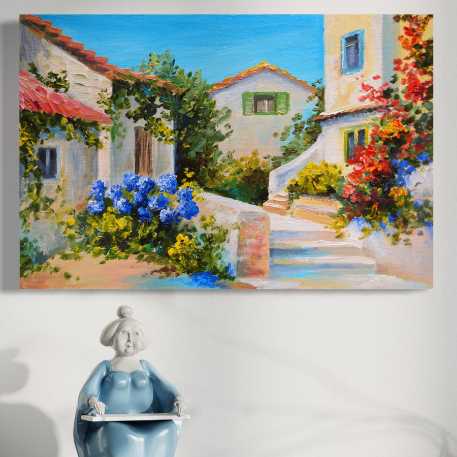 O pânză LuxCanva® Tablou Canvas Premium A1079, Casa Cu Flori cu culori vibrante și peisaje naturale atârnă deasupra unei figurine din ceramică albastră și albă a unei femei care citește pe un perete alb.