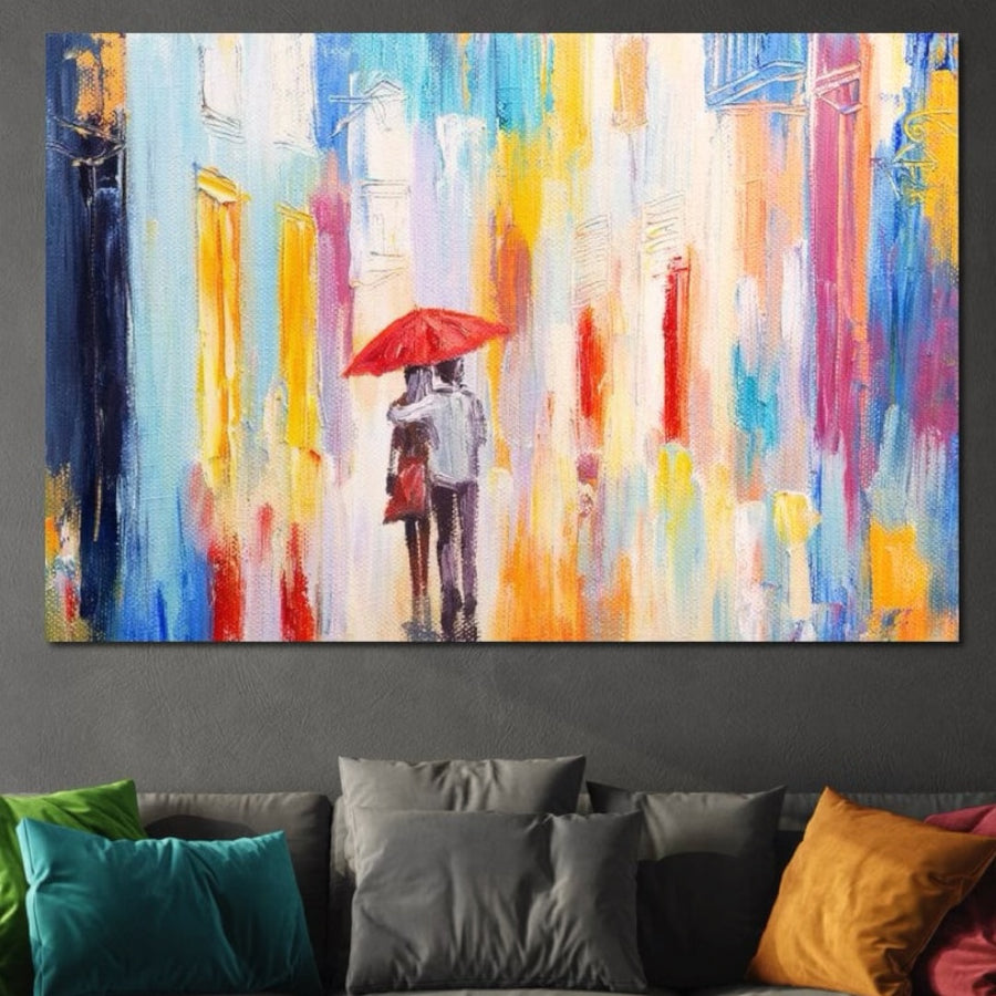 Deasupra unei canapele gri cu perne verzi, galbene, portocalii și maro este agățat tabloul LuxCanva® Tablou Canvas Premium LuxCanva® E1035, reprezentând o scenă urbană vibrantă cu un cuplu care împarte o umbrelă roșie în "Ploaie Romantică".