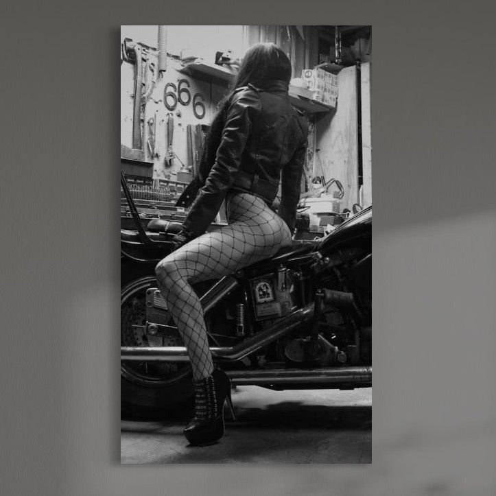 tablou canvas cu o femeie cu dresuri tip plasa pe o motocicleta , intr-un garaj redat in nuante de alb si negru