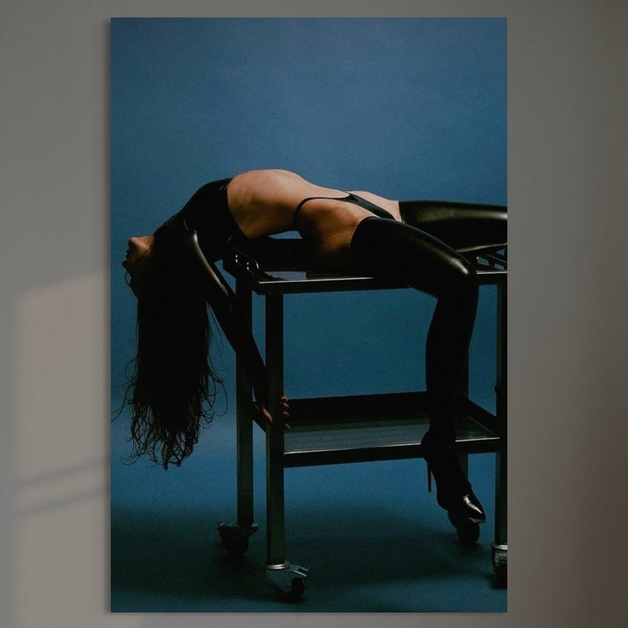 Tablou Canvas Premium LuxCanva® P1057 cu o persoană în lenjerie neagră și cizme, spectaculos arcuită peste o masă metalică pe fund albastru, surprinde echilibrul și senzualitatea - ideal pentru decor living sau dormitor.