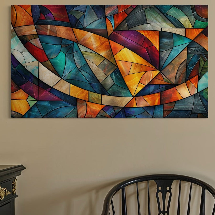 Tabloul LuxCanva® Premium Canvas Tablou C1287, cu modele geometrice abstracte de mozaic în tonuri vibrante de albastru, portocaliu, roșu, galben și verde, este agățat deasupra unui scaun negru și a unui dulap pe un perete bej - ideal pentru camera de zi sau decor de birou.