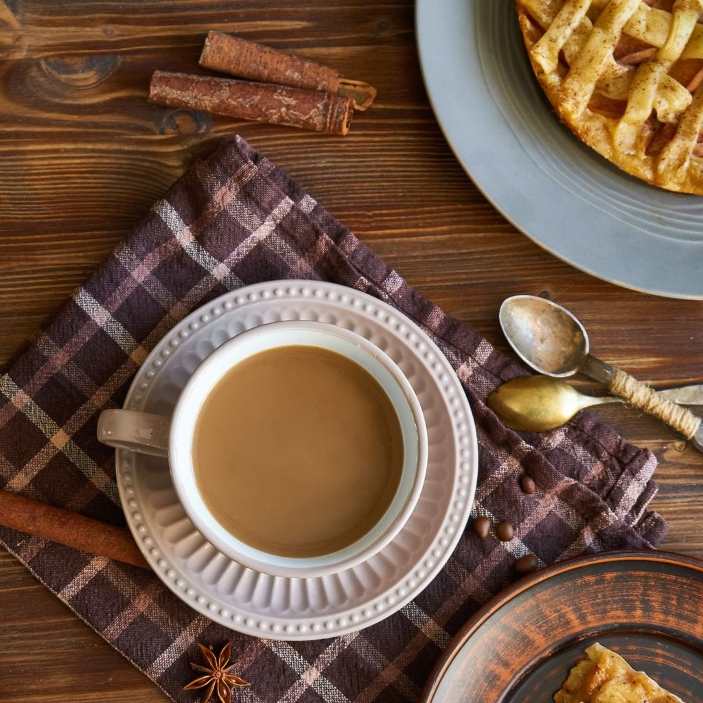 tablou canvas cu o ceasca de cafea, pe o masa de lemn cu farfurii cu placinta si tacamuri de mic dejun, intr-un cadru rustic 
