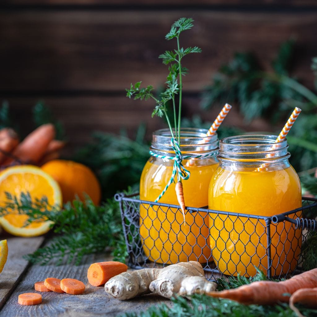 tablou canvas cu doua pahare cu suc de portocale si morcovi, cu paie colorate, pe fundal rustic de lemn cu fructe si legume