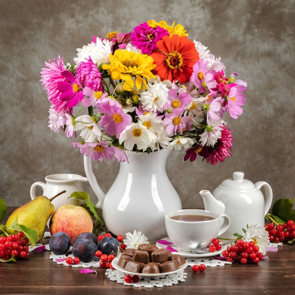 tablou canvas cu o vaza cu flori colorate, pe o masa de lemn cu o ceasca de cafea, fructe si praline de ciocolata