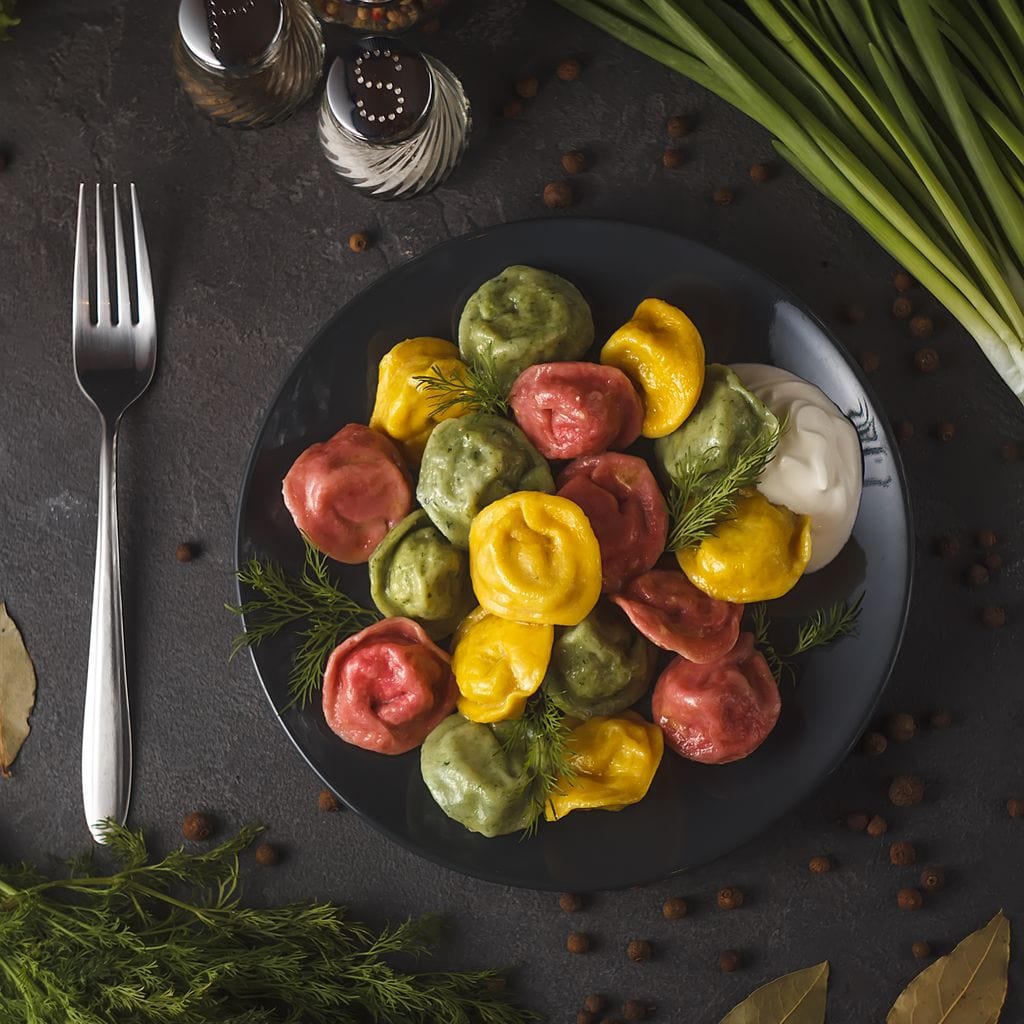 tablou canvas cu o portie de ravioli pe o farfurie neagra, pe o masa cu mirodenii si tacamuri