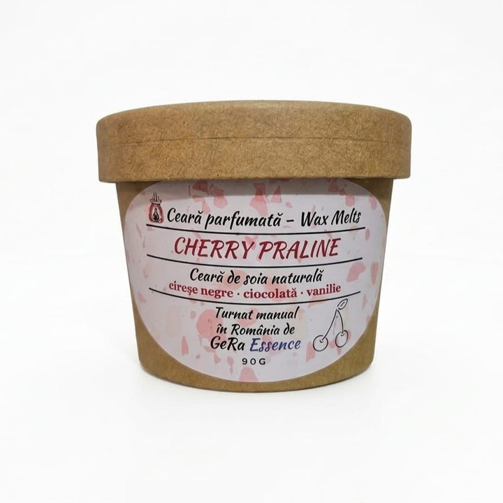 Un recipient LuxCanva® din hârtie maro etichetat "Cherry Praline" conține 90 g de topituri din ceară de soia realizate manual, cu note gurmande de cireșe negre, ciocolată, vanilie și esență GeRa. Textul este în limba română: ceara naturala parfumata.